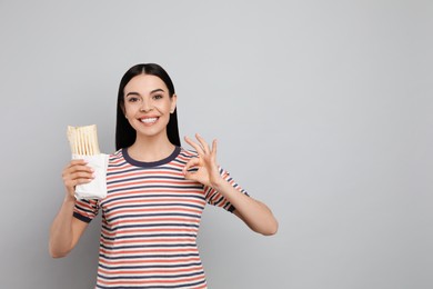 Happy young woman with delicious shawarma on grey background. Space for text