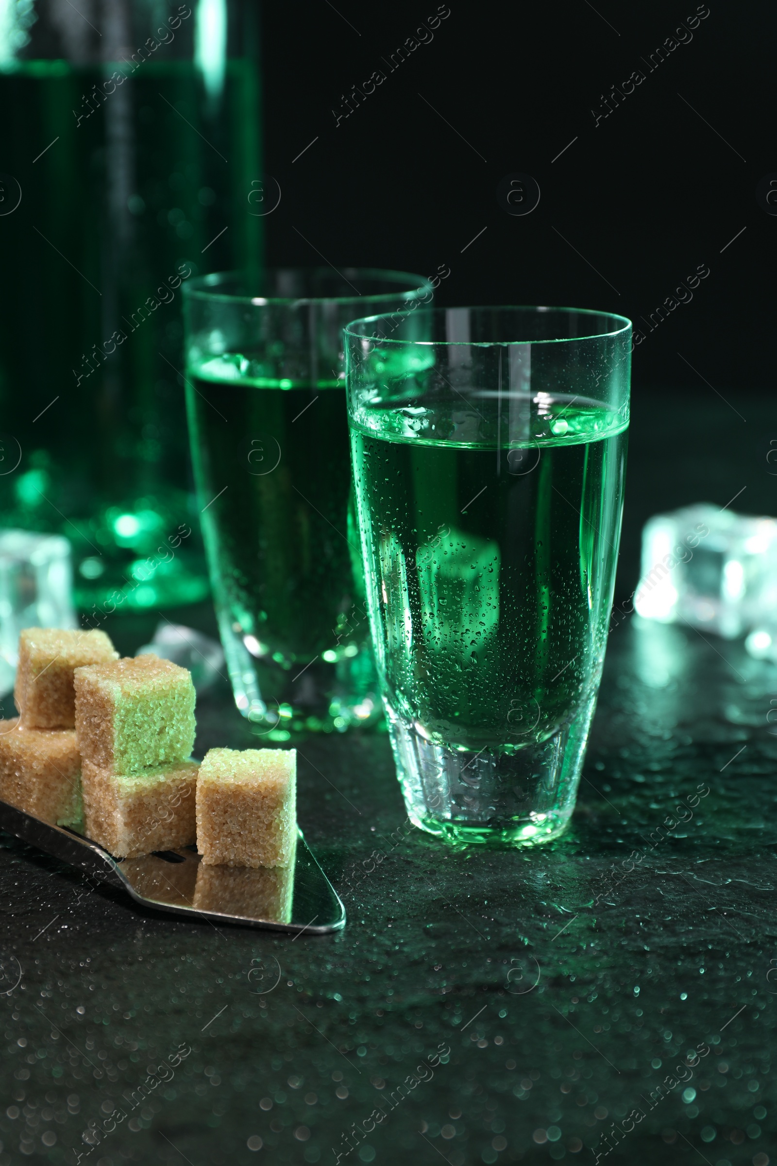 Photo of Absinthe in shot glasses, spoon and brown sugar cubes on gray table, closeup. Alcoholic drink