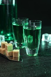 Absinthe in shot glasses, spoon and brown sugar cubes on gray table, closeup. Alcoholic drink
