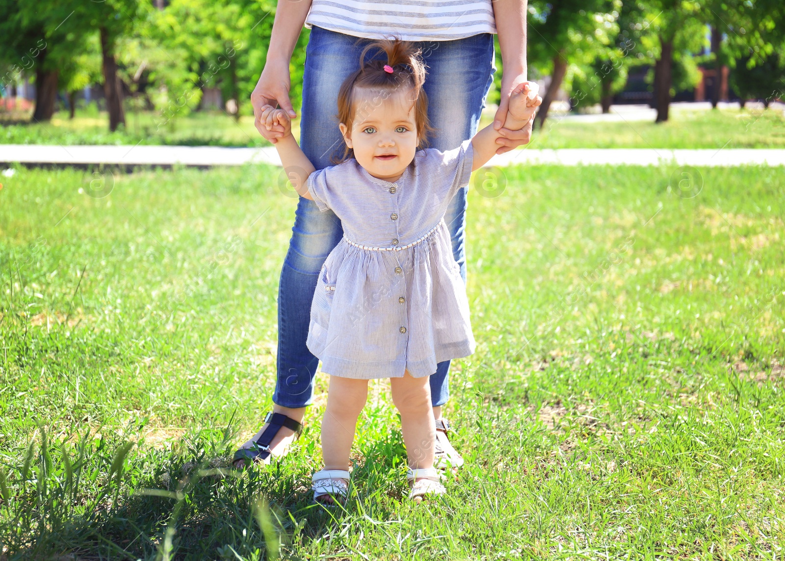 Photo of Adorable baby girl holding mother's hands while learning to walk outdoors