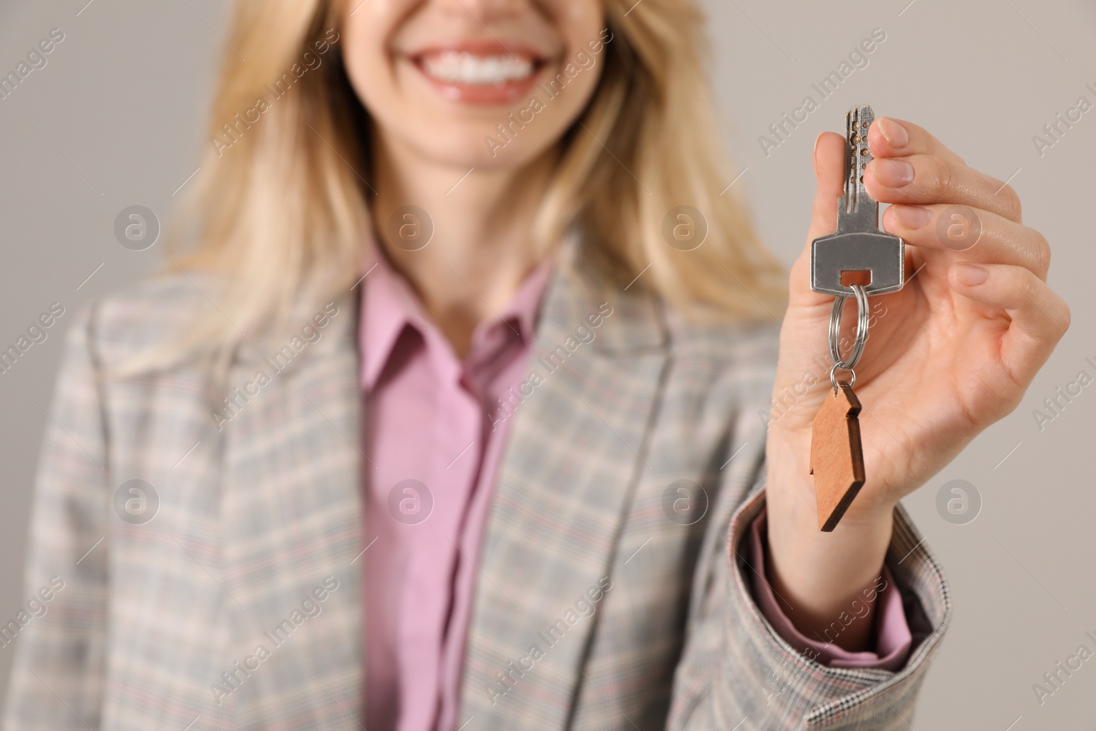 Photo of Real estate agent holding key against grey background, closeup