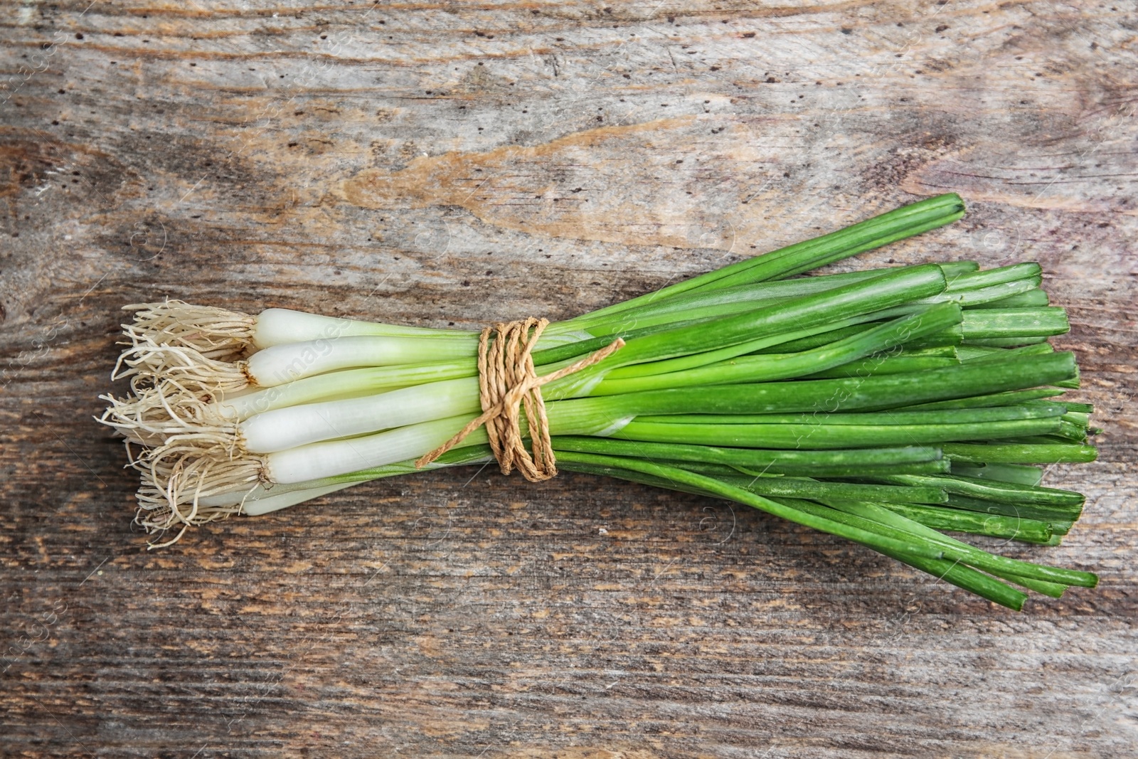 Photo of Tied fresh green onion on wooden table, top view