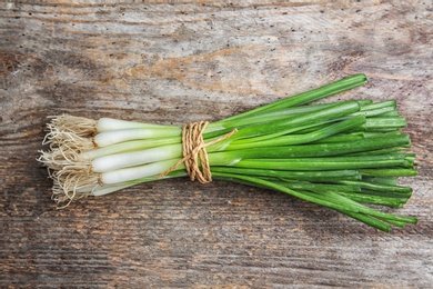 Photo of Tied fresh green onion on wooden table, top view