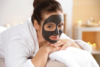 Photo of Beautiful woman with black mask on face relaxing in spa salon