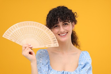 Photo of Happy woman holding hand fan on orange background