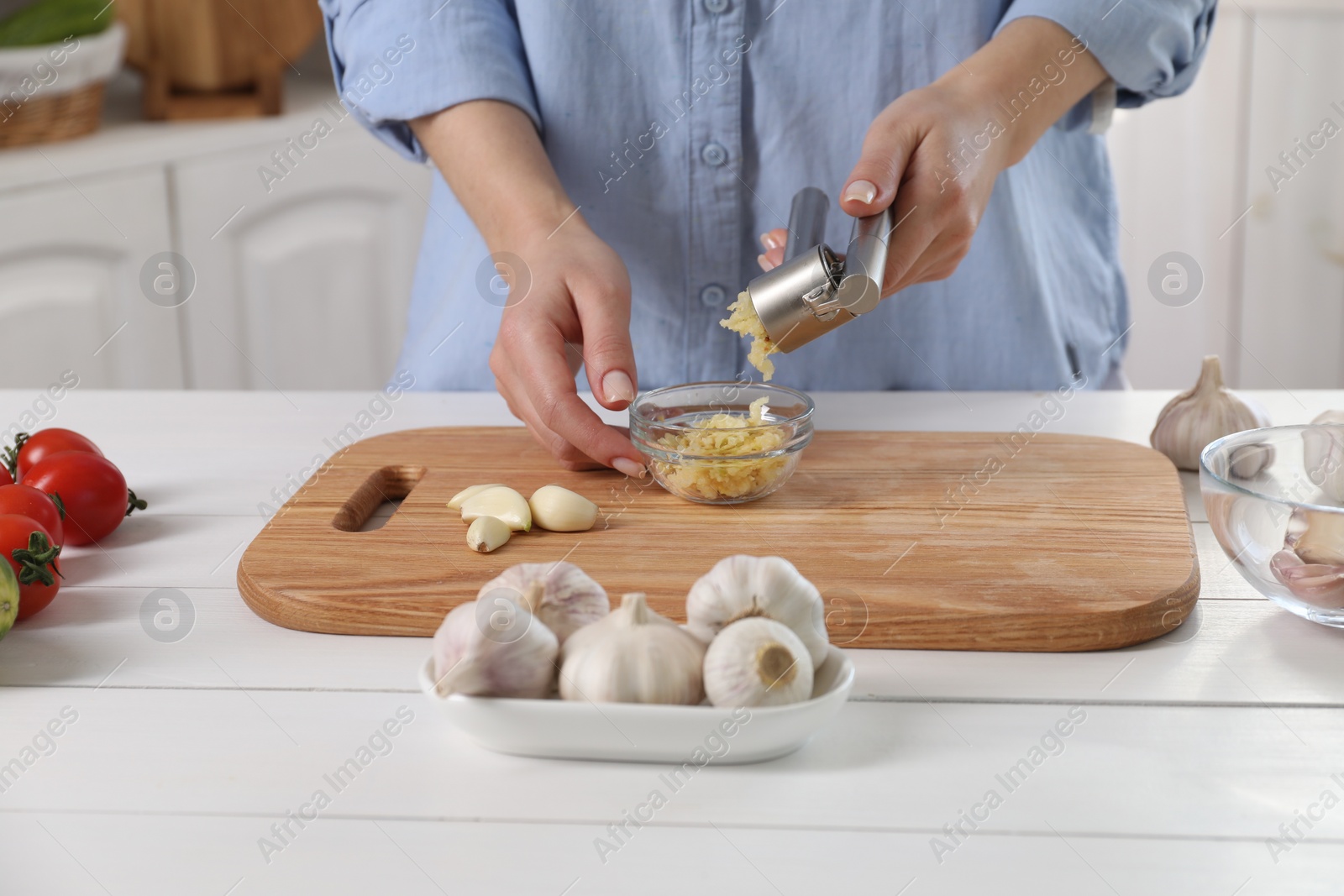 Photo of Woman squeezing garlic with press at white wooden table in kitchen, closeup