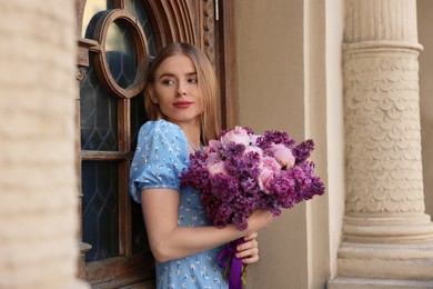 Beautiful woman with bouquet of spring flowers near building outdoors