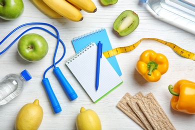 Flat lay composition with notebooks, healthy food and jumping rope on wooden background. Weight loss concept