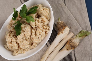 Photo of Bowl of tasty prepared horseradish and roots on table, closeup
