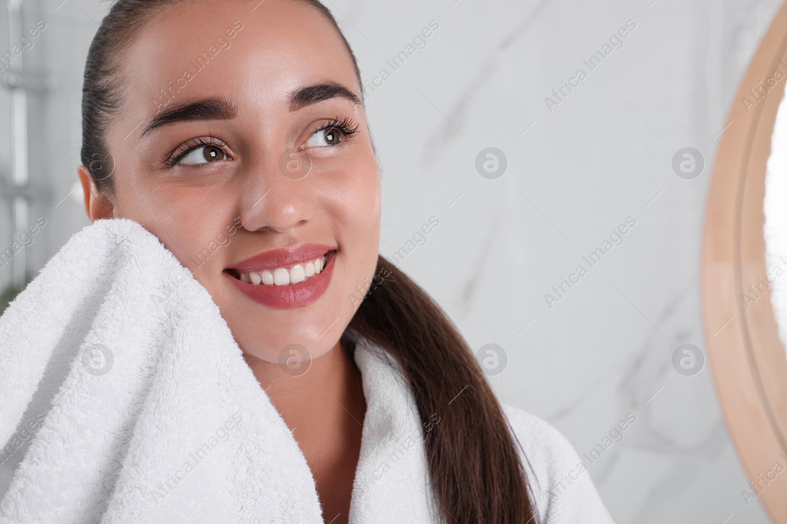 Photo of Beautiful young woman wiping face with towel in bathroom, closeup. Facial wash