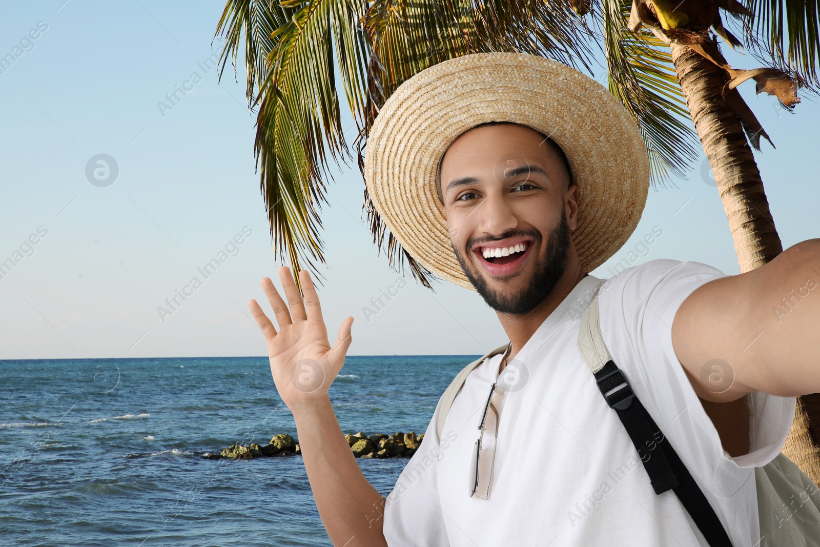 Image of Smiling young man in straw hat taking selfie at tropical resort