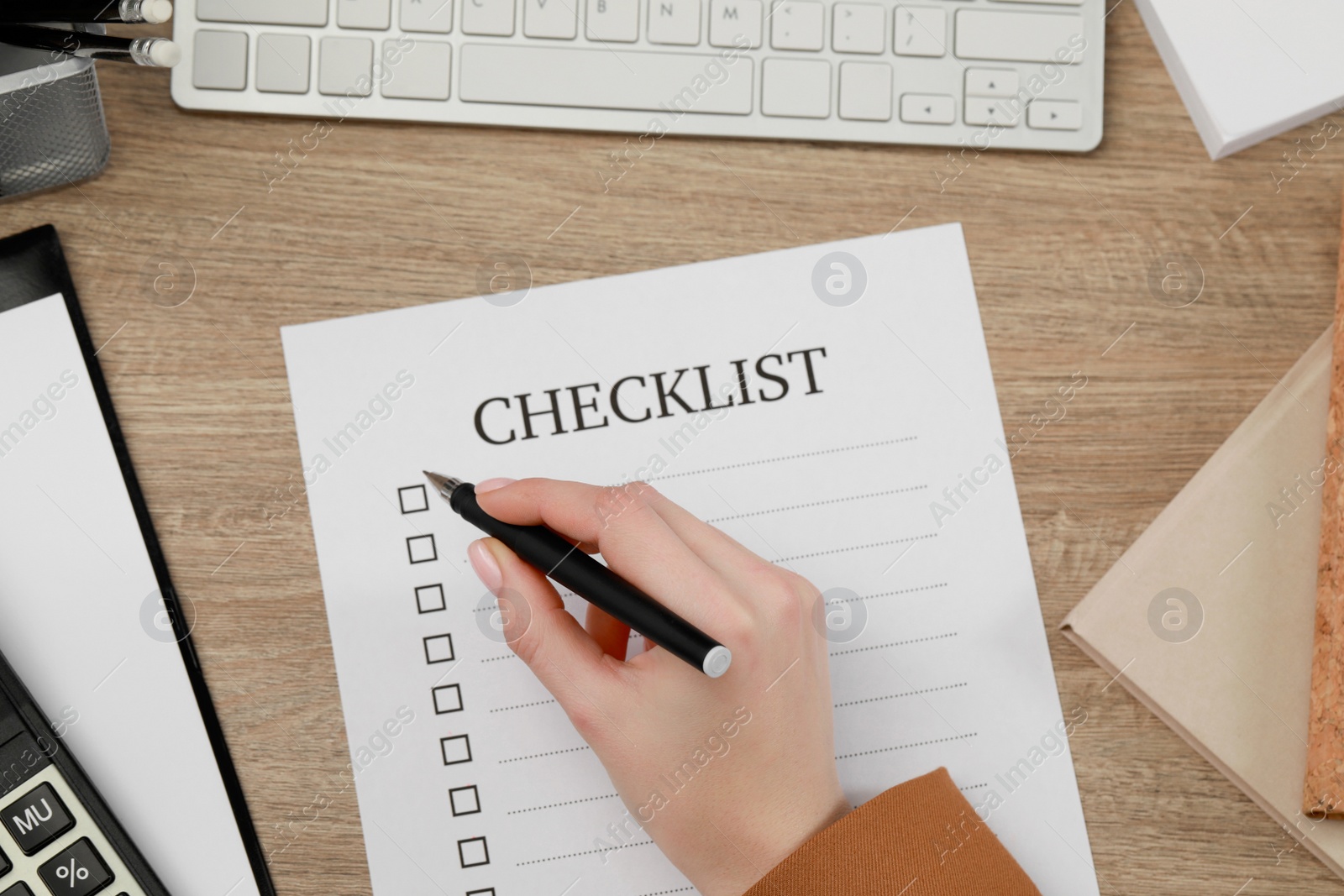 Photo of Woman filling Checklist at wooden table, top view
