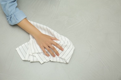 Photo of Woman wiping grey table with kitchen towel, top view. Space for text