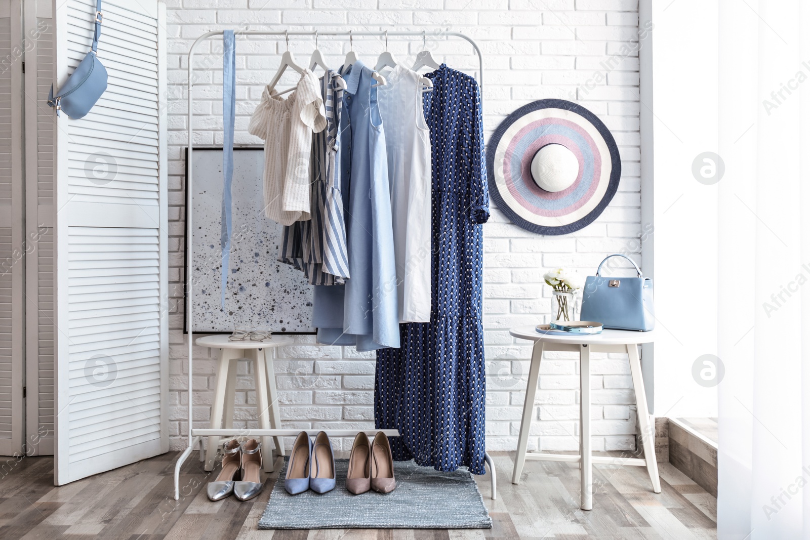 Photo of Wardrobe rack with women's clothes and different shoes at white brick wall in room