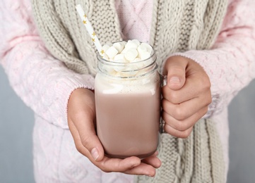 Photo of Woman holding mason jar of delicious cocoa drink with marshmallows, closeup