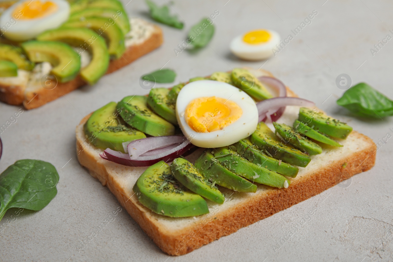 Photo of Tasty toast with avocado and quail egg served on light grey table, closeup