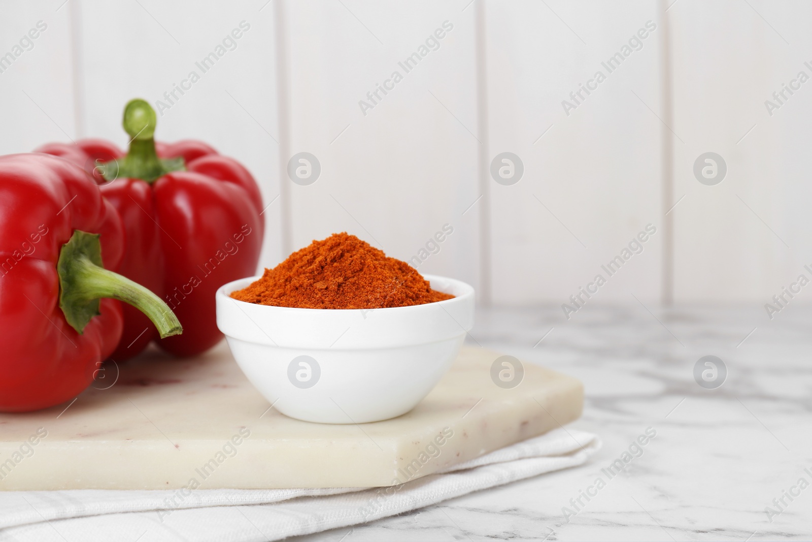 Photo of Bowl with aromatic paprika powder and fresh bell peppers on white marble table. Space for text