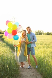 Photo of Young couple with colorful balloons in field on sunny day