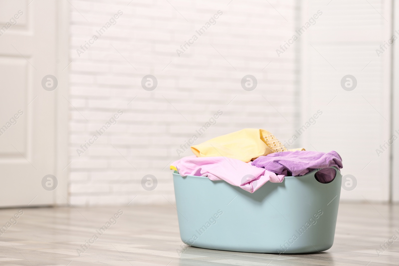 Photo of Laundry basket with dirty clothes on floor indoors. Space for text