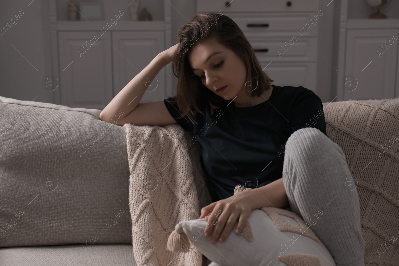 Photo of Sad young woman sitting on sofa at home