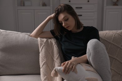 Photo of Sad young woman sitting on sofa at home