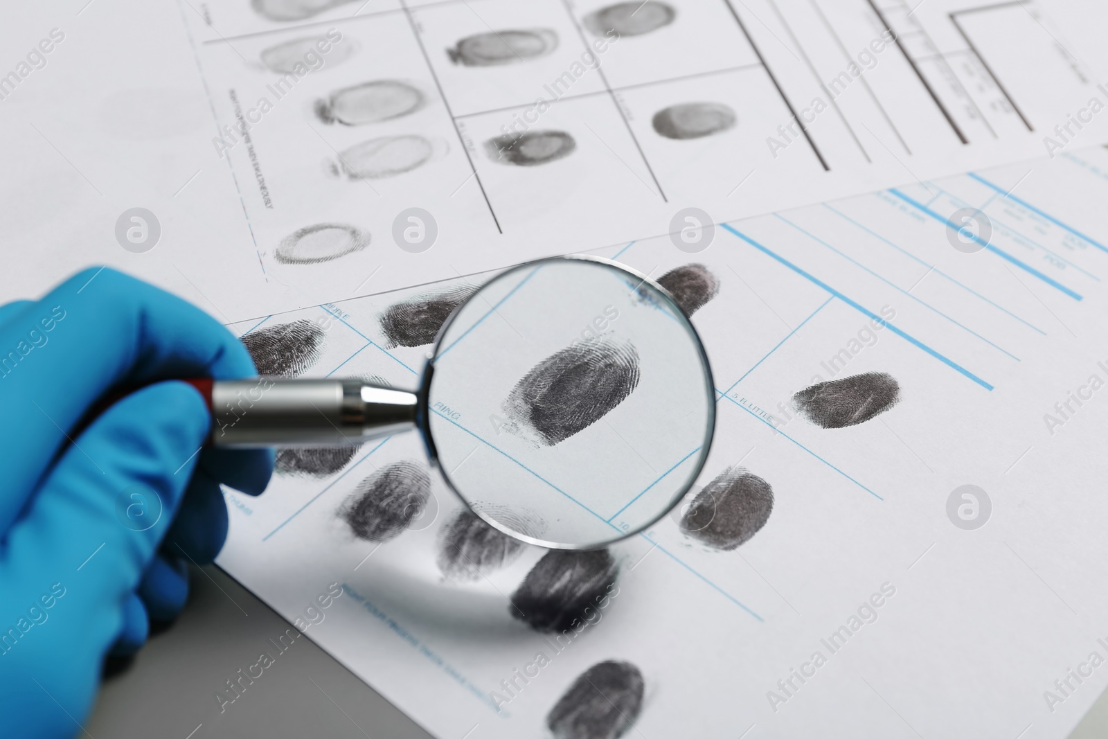 Photo of Criminalist exploring fingerprints with magnifying glass, closeup