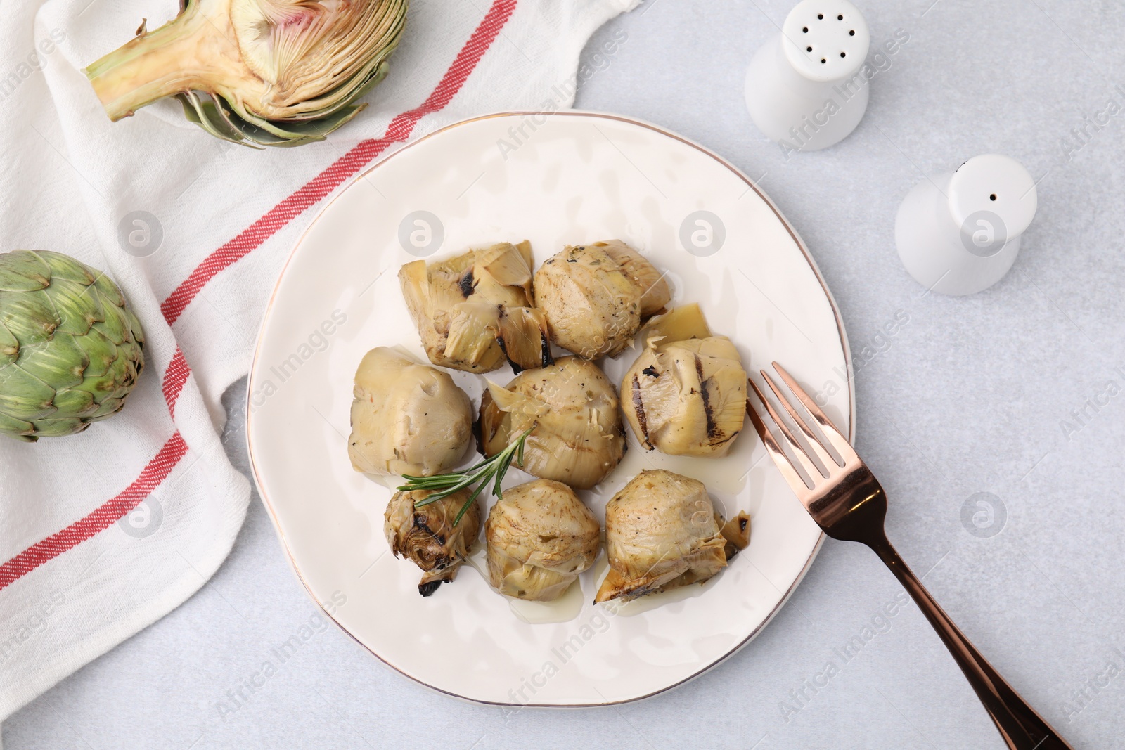 Photo of Delicious pickled artichokes with rosemary served on light grey table, flat lay