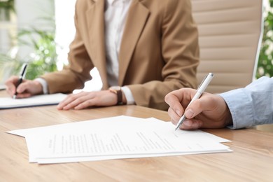 Photo of Man signing contract at table in office, closeup.