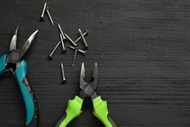 Pliers and nails on black wooden table, flat lay. Space for text