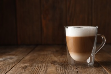 Photo of Hot coffee with milk in glass cup on wooden table. Space for text