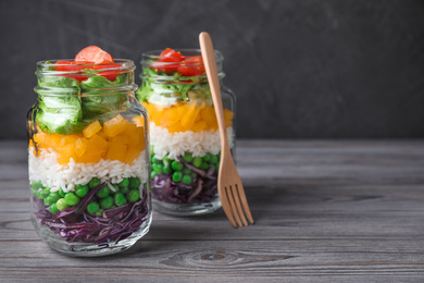 Photo of Healthy salad in glass jars on grey wooden table. Space for text