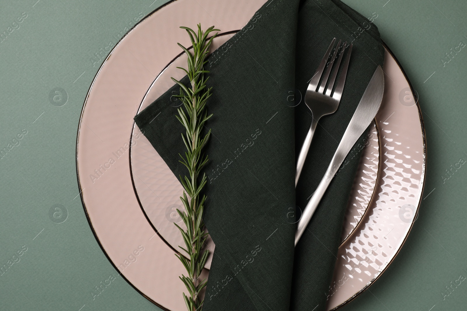 Photo of Stylish table setting. Plates, cutlery, napkin and rosemary on green background, top view
