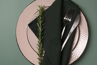 Stylish table setting. Plates, cutlery, napkin and rosemary on green background, top view