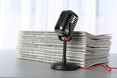 Newspapers and vintage microphone on grey table. Journalist's work