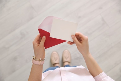 Photo of Woman holding envelope and blank greeting card indoors, top view