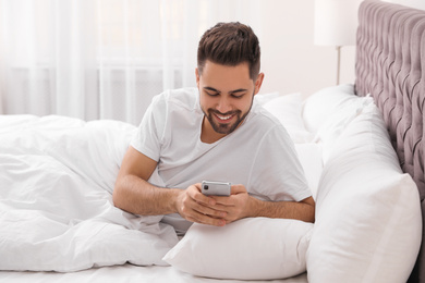 Young man addicted to smartphone in bed at home