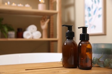 Dispensers of liquid soap, burning candle and eucalyptus branch on bath tray indoors. Space for text