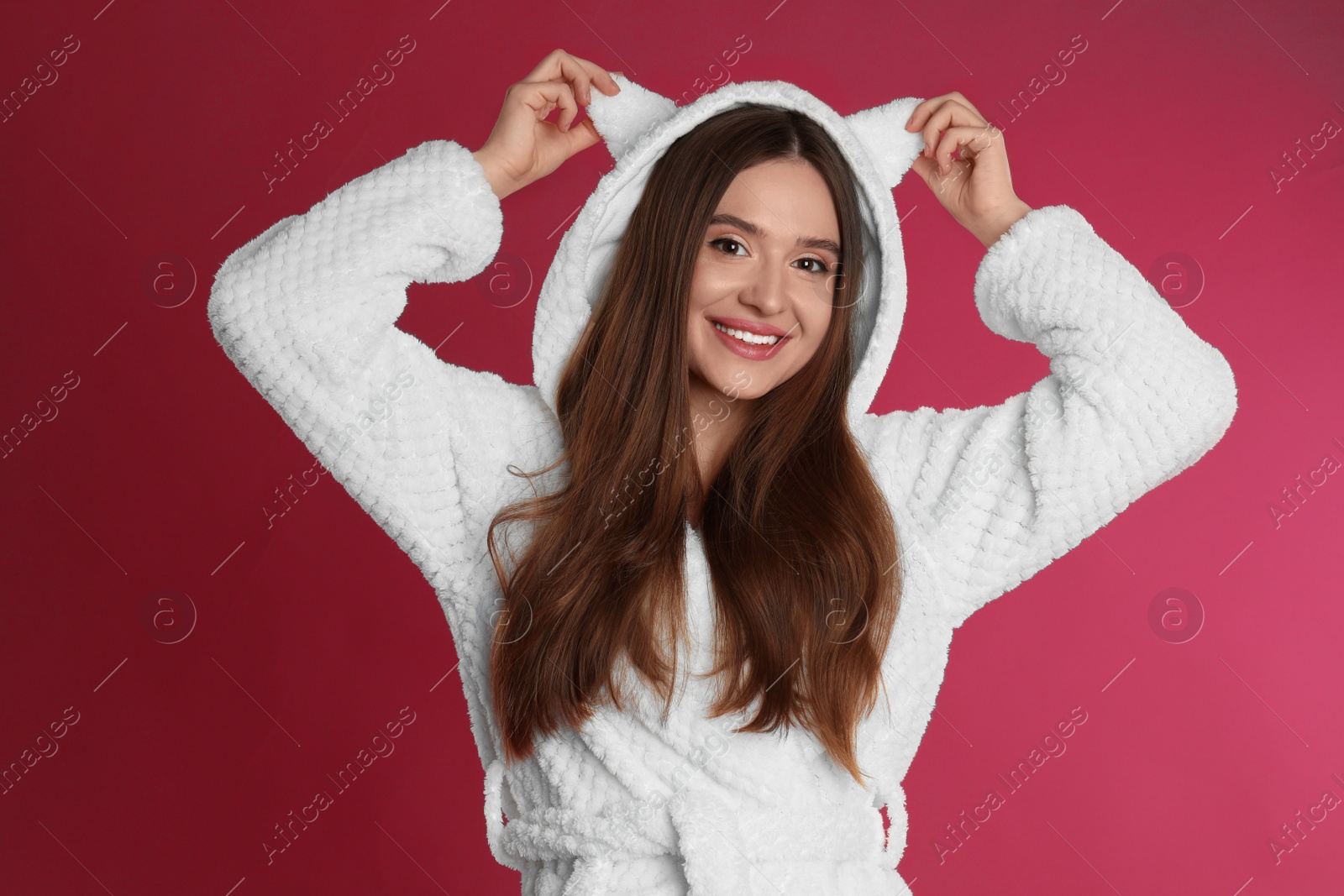 Photo of Young woman in bathrobe with funny hood on crimson background