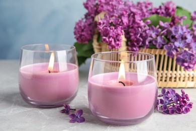 Photo of Burning wax candles in glass holders and lilac flowers on grey table