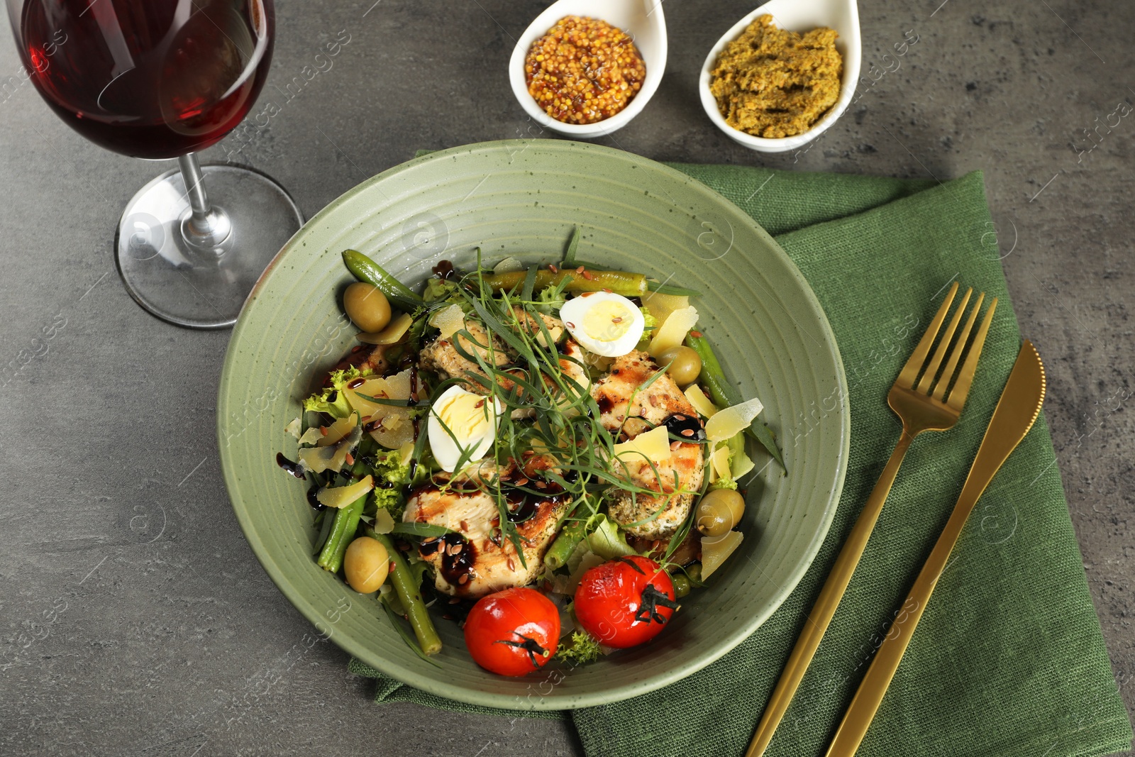 Photo of Tasty dish with tarragon, salad dressings and glass of wine served on grey table, above view