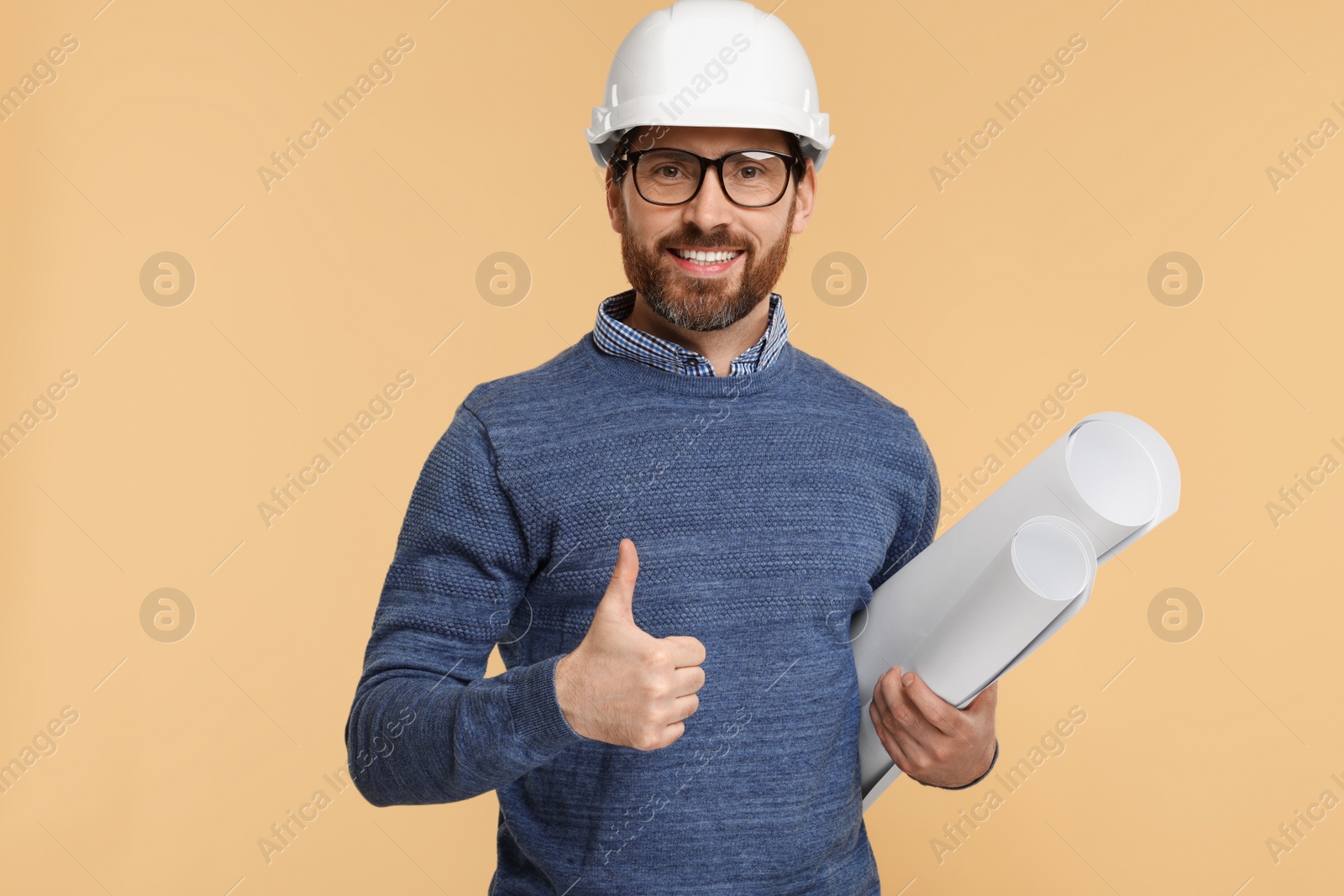 Photo of Architect in hard hat with drafts showing thumbs up on beige background