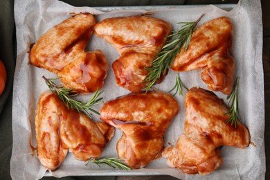 Photo of Raw marinated chicken wings and rosemary on table, top view