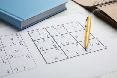 Photo of Sudoku, pen and planner on white table, closeup