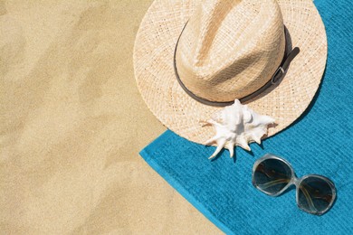 Soft blue beach towel, sunglasses, straw hat and seashell on sand, flat lay. Space for text