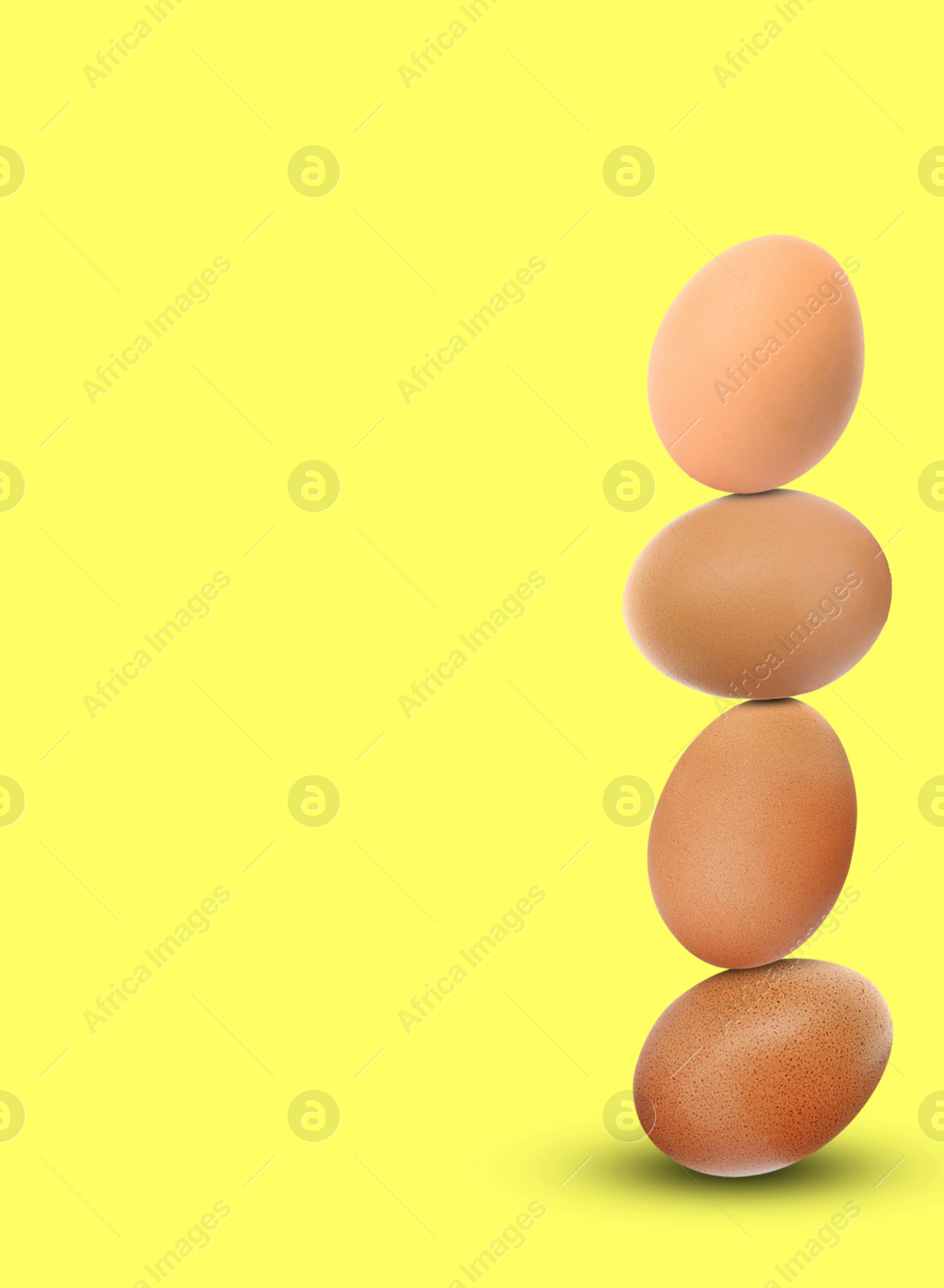 Image of Stacked fresh chicken eggs against light yellow background. Space for text