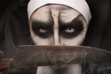 Scary devilish nun with knife on black background, closeup. Halloween party look