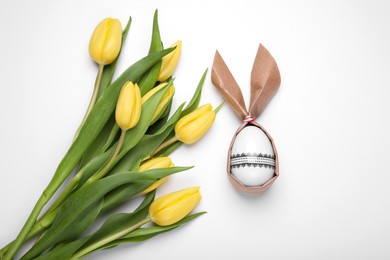 Photo of Easter bunny made of craft paper and egg near beautiful tulips on white background, flat lay