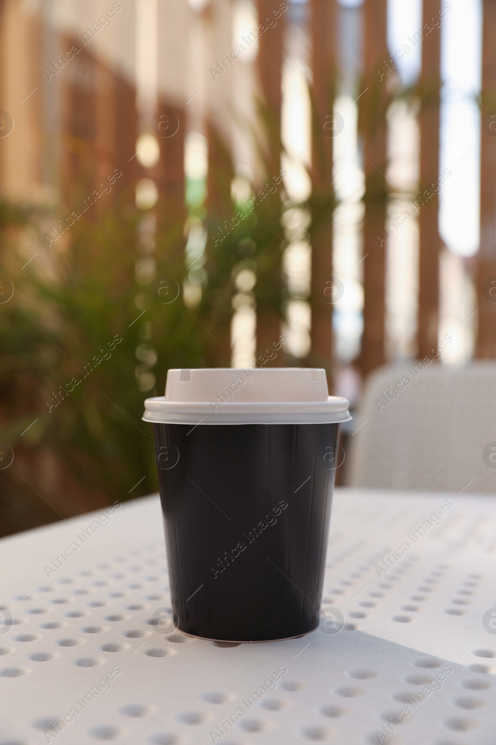 Photo of Takeaway paper cup with plastic lid on white table indoors