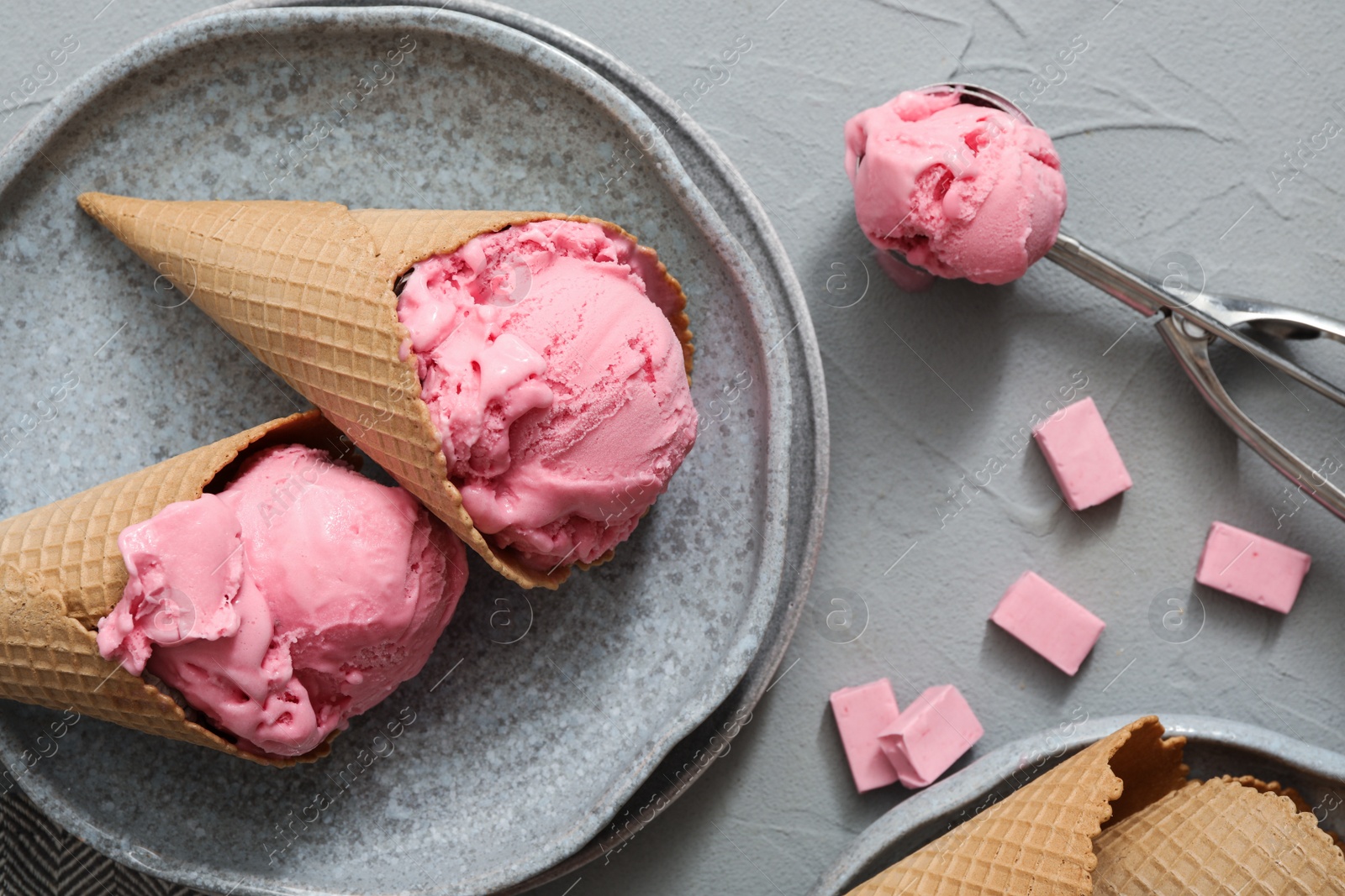 Photo of Delicious pink ice cream in wafer cones with candies on grey table, flat lay