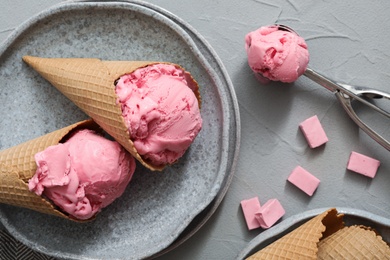 Photo of Delicious pink ice cream in wafer cones with candies on grey table, flat lay